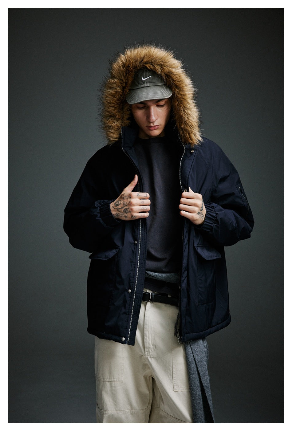 Front view of a model holding open a navy fur-trimmed parka, showing its zipper and front pockets.