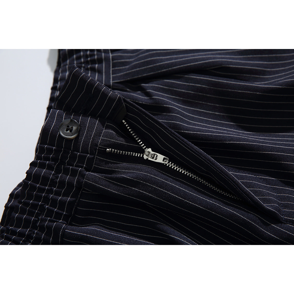 Close-up of dark pinstripe shorts with the fly unzipped, showing a metal zipper and waistband button.