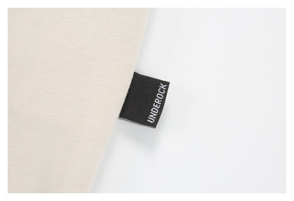 Close-up of an UNDER ROCK fabric label sewn into the edge of off-white material.
