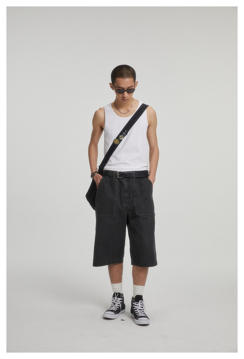 Model wearing a white tank top and loose black knee-length shorts with large front patch pockets.