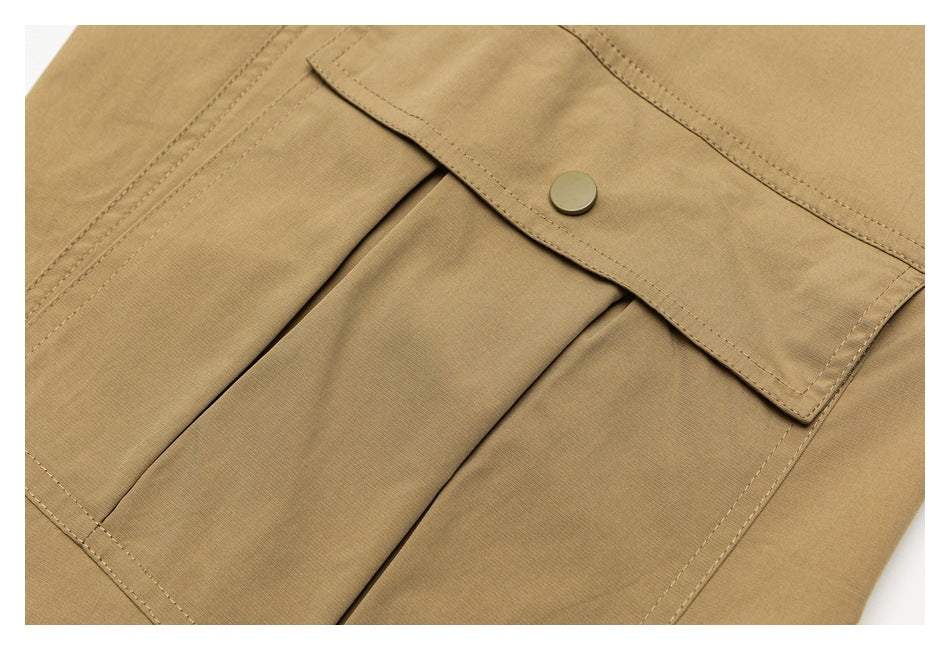Close-up of tan garment fabric with a stitched flap, snap button, and pleated panels.