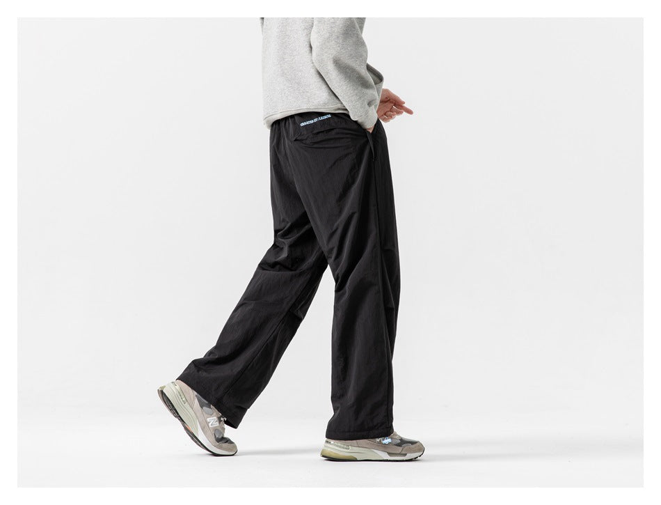 Rear-side view of a model wearing loose black pants with a small back pocket and sneakers.