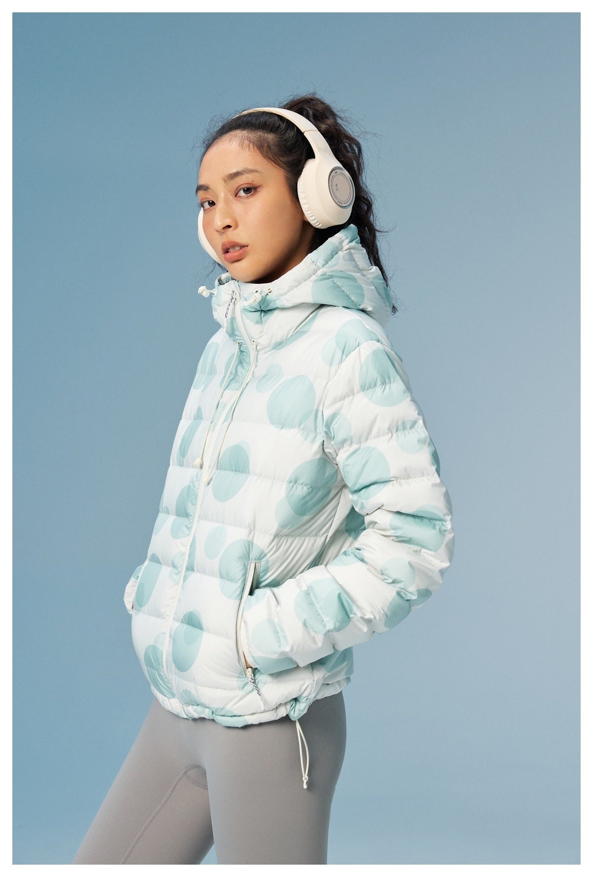 Three-quarter side view of a model wearing a white hooded puffer jacket with pale aqua circles.