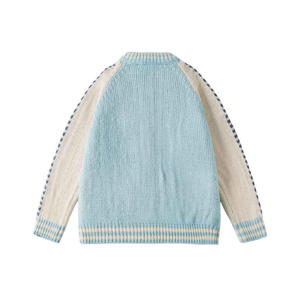 Back of a pale blue knit cardigan with cream raglan sleeves, navy patterned edges, and pale striped ribbed trim.