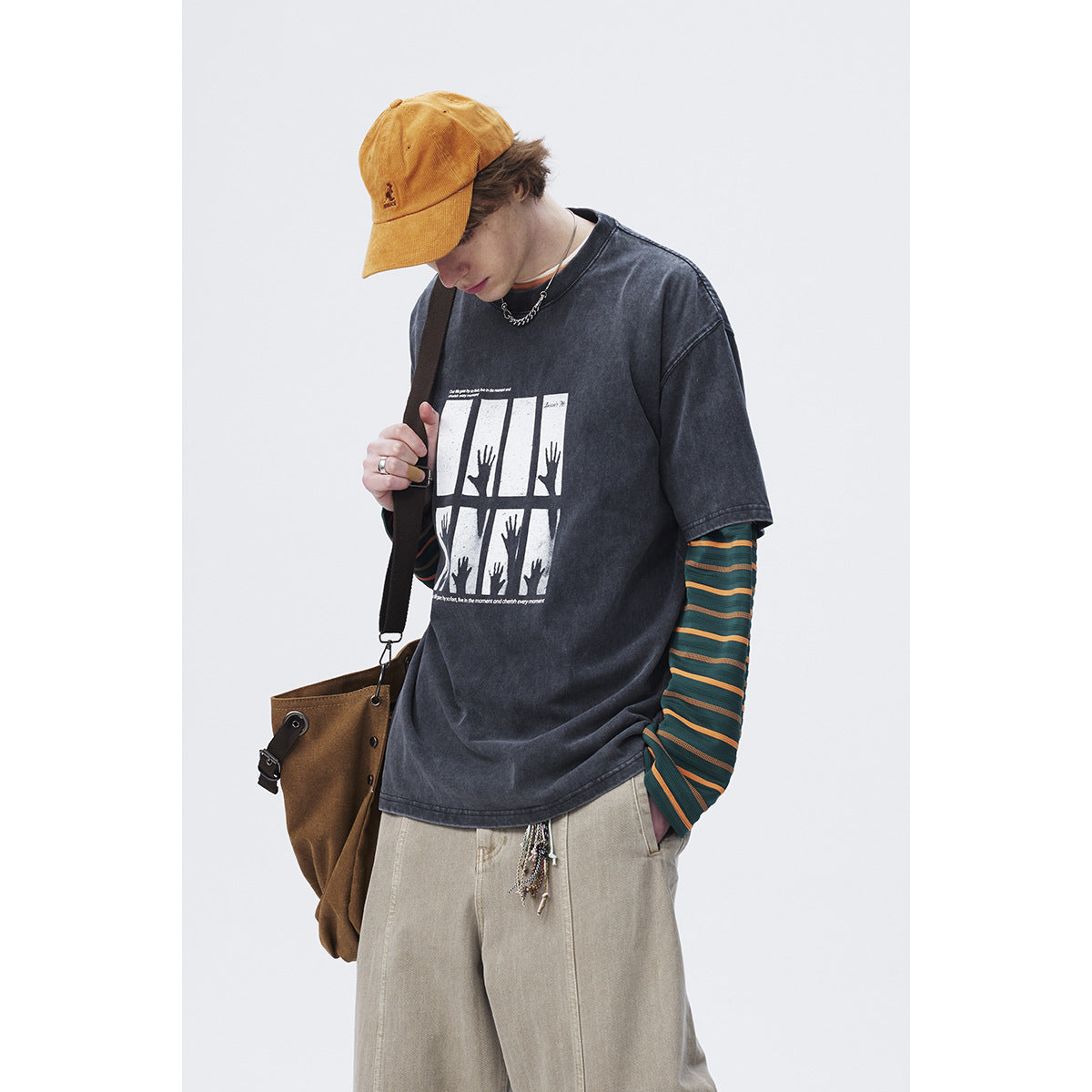 Model wearing an oversized charcoal graphic T-shirt over a green-and-orange striped long-sleeve shirt.