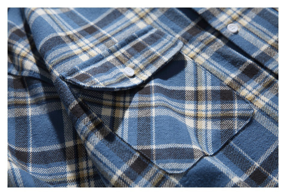Close-up of a flap pocket and white button on a blue plaid shirt.