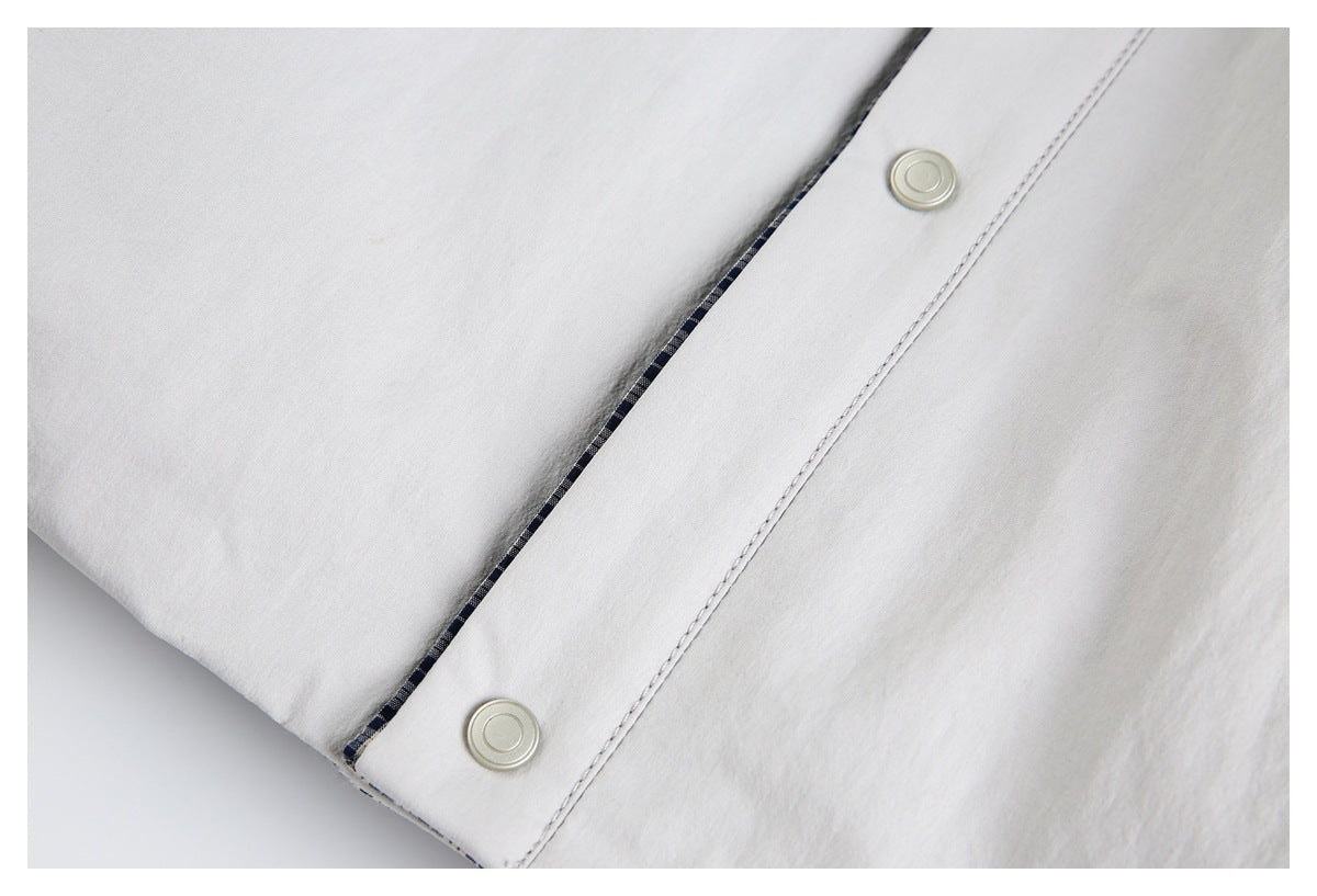 Close-up of a pale gray garment placket with two silver snap fasteners and narrow navy plaid trim.