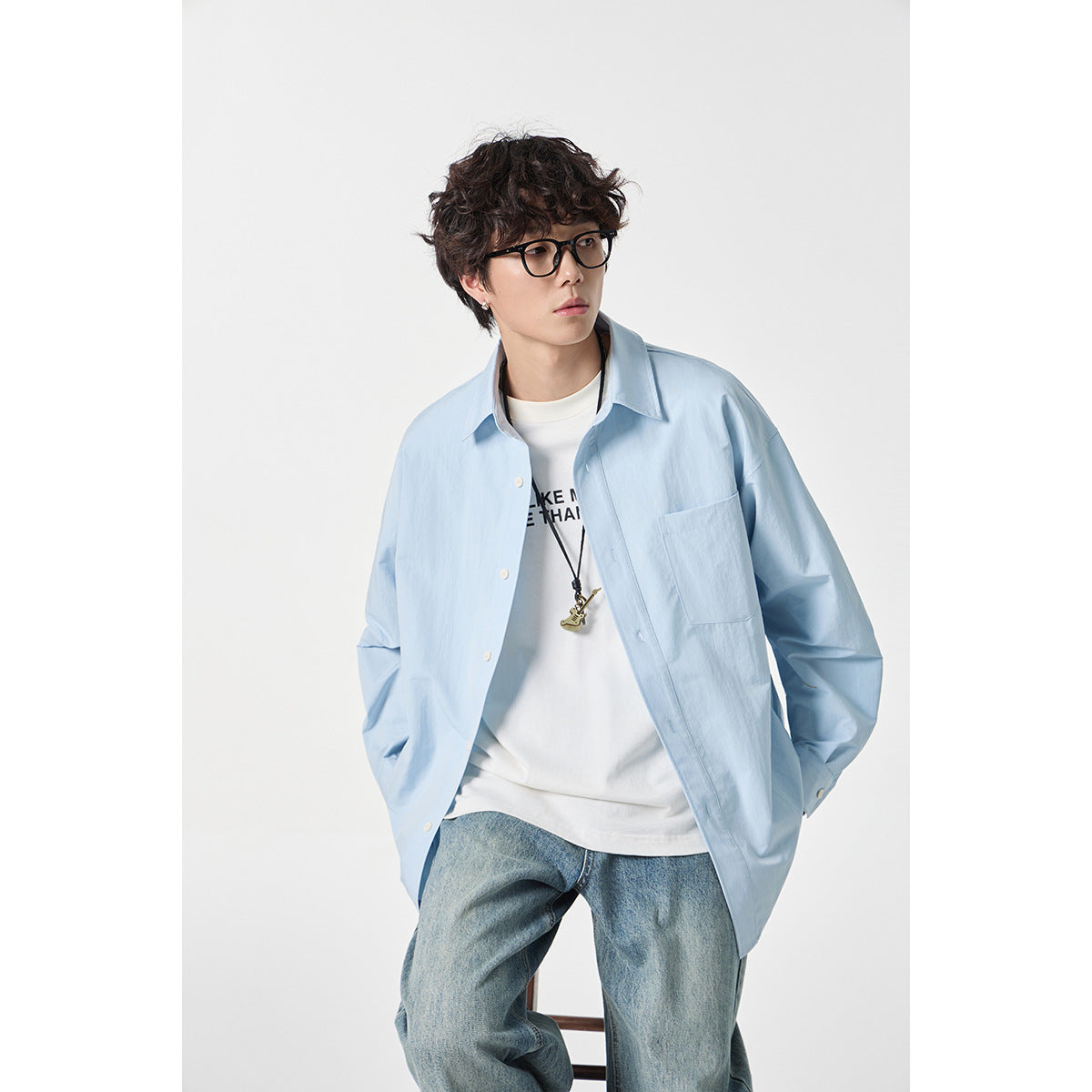 Closer front view of a model wearing an oversized light blue button-up shirt with a chest pocket over a white tee.