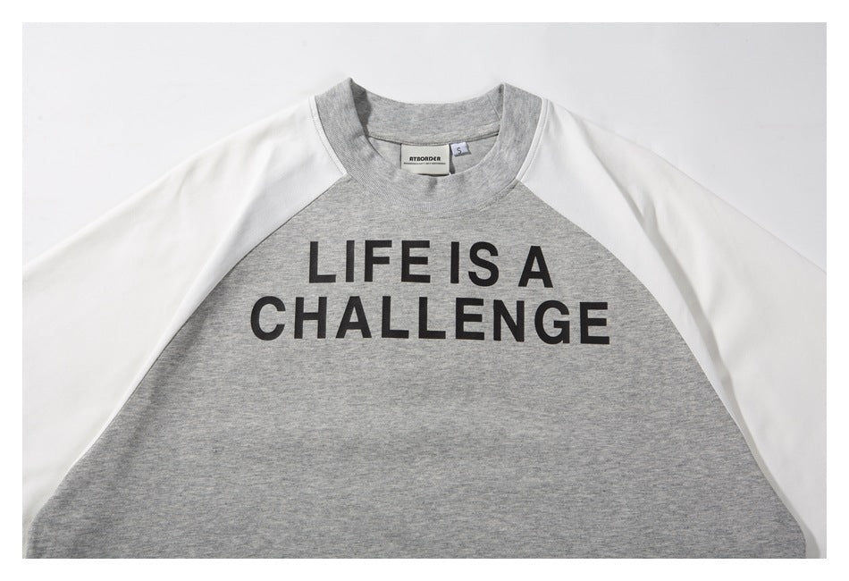 Flat-lay front of a gray raglan sweatshirt with white sleeves and black “LIFE IS A CHALLENGE” lettering.