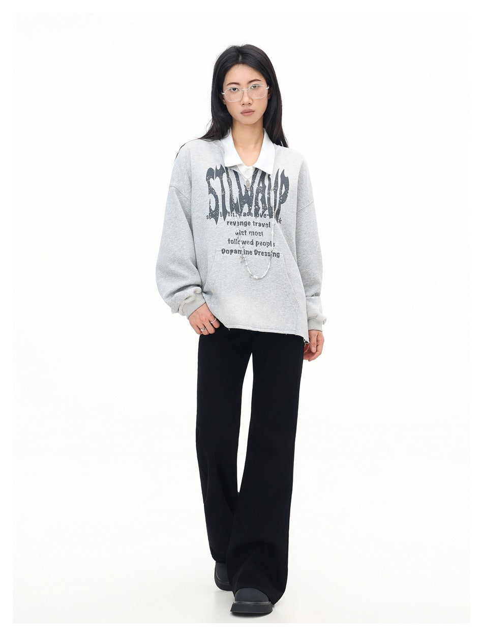 Model wearing a light gray graphic pullover layered over a white collared shirt, with black wide-leg pants.