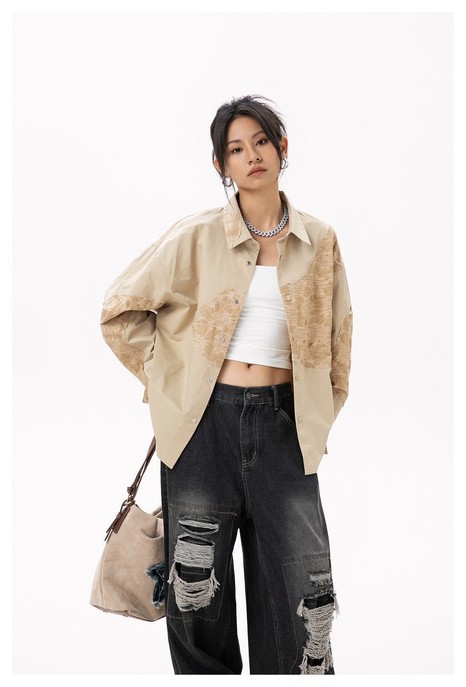 Model wearing a beige oversized button-up shirt with tan textured panels and distressed black jeans.