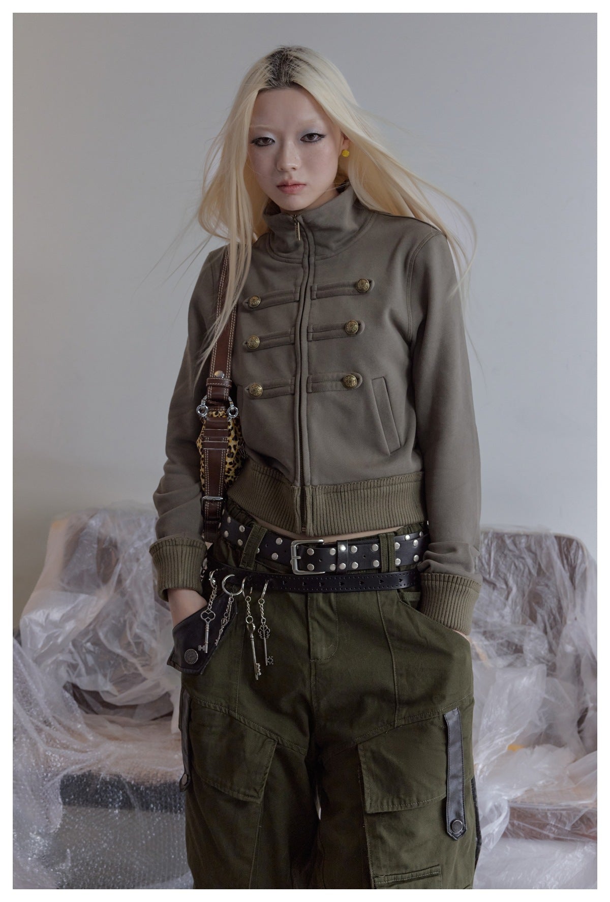 Model wearing a taupe high-collar jacket with brass button tabs and olive cargo pants.