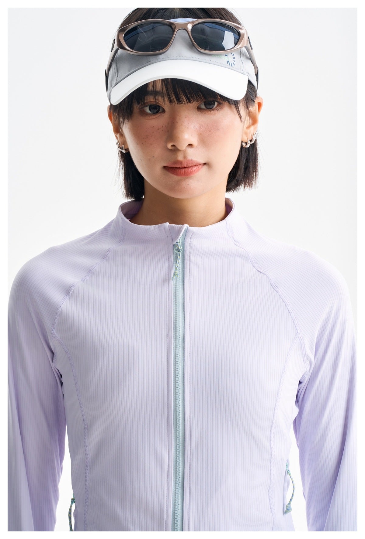 Close-up of a pale lavender ribbed jacket with a mint zipper and curved seam detailing, worn by a model.