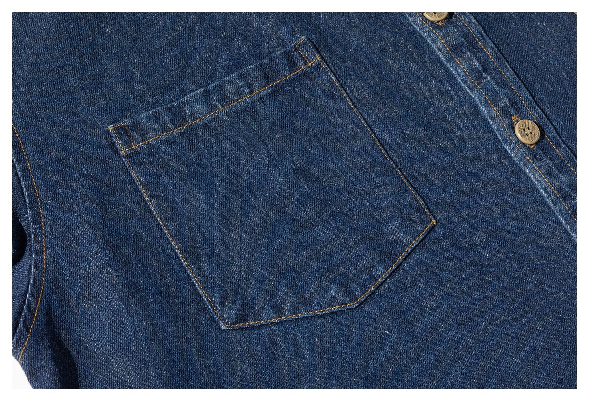 Close-up of a plain patch pocket on a dark blue denim shirt with contrasting stitching and a wooden-look button.