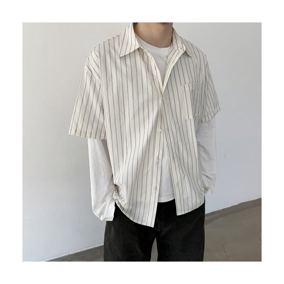 Person wearing an off-white short-sleeve button-up shirt with thin vertical stripes over a white long-sleeve top.
