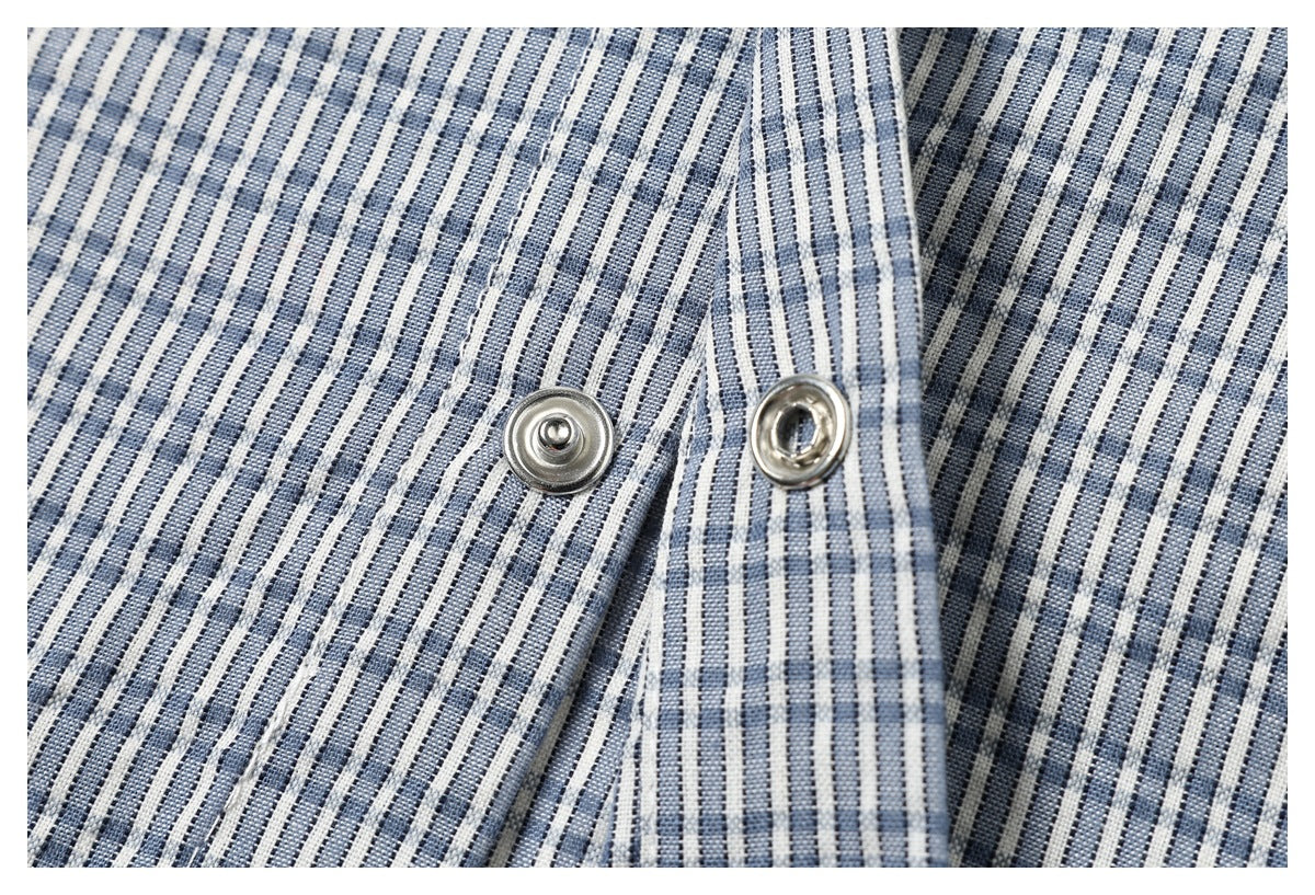 Close-up of two metal snap fasteners on blue-and-white striped garment fabric.