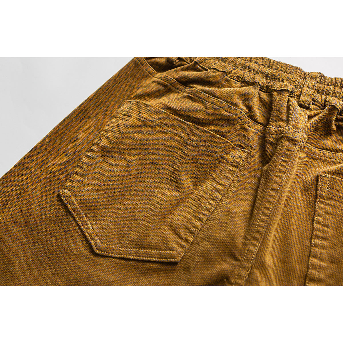 Close-up of ochre pants showing a rear patch pocket, elastic waistband, and belt loop.