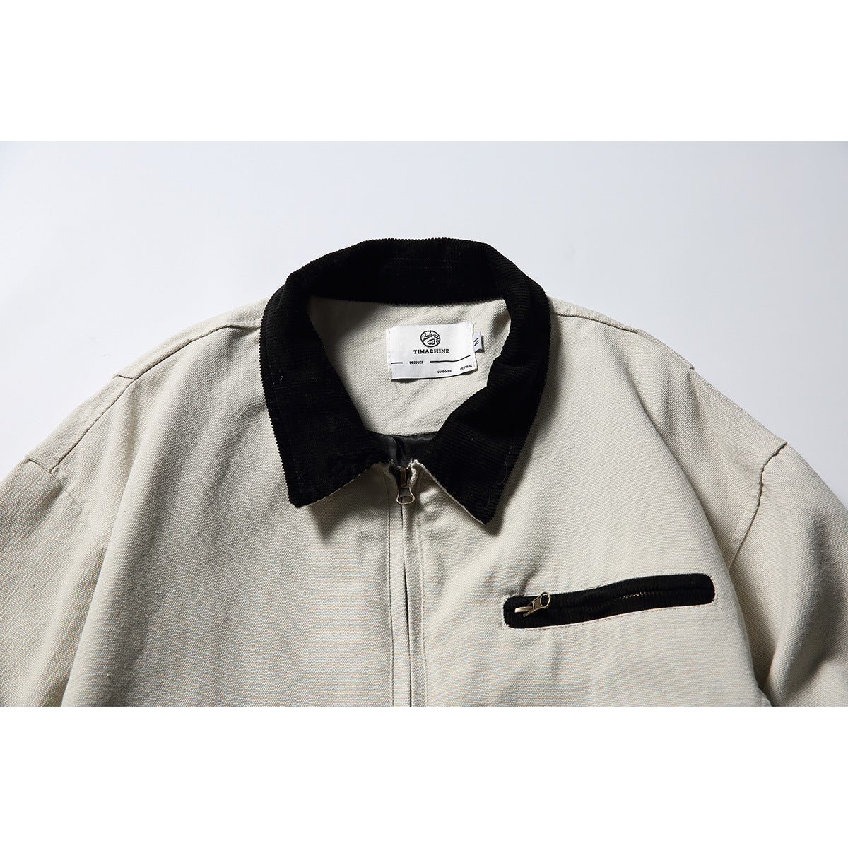 Close-up of an off-white jacket front with a black collar, center zipper, and black-trimmed chest zipper pocket.