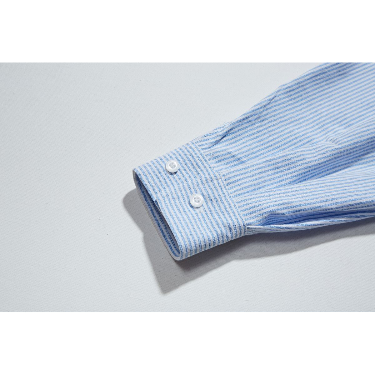 Close-up of a blue-and-white striped shirt sleeve and buttoned cuff.