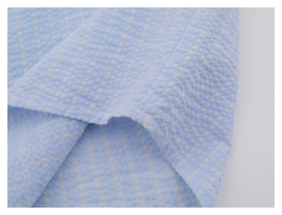 Close-up of the stitched lower edge and overlapping fabric of a light blue subtly checked shirt.