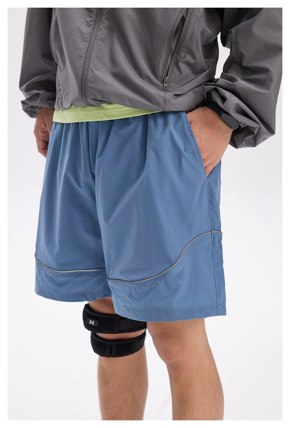 Close-up of blue athletic shorts showing a side pocket, curved contrast piping, and wide hem.