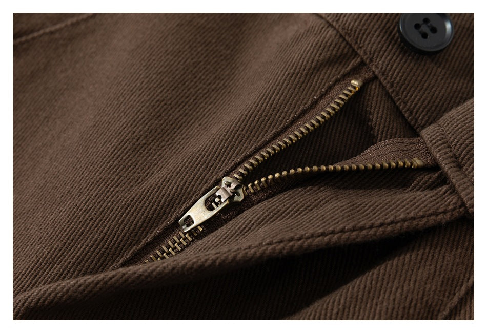 Close-up of a metal zipper and black button on brown trousers.