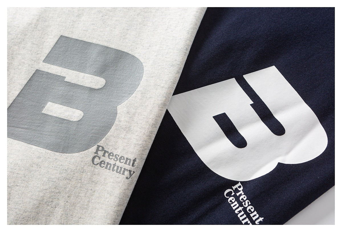 Close-up of heather gray and navy T-shirts showing large contrasting B prints with small “Present Century” text.