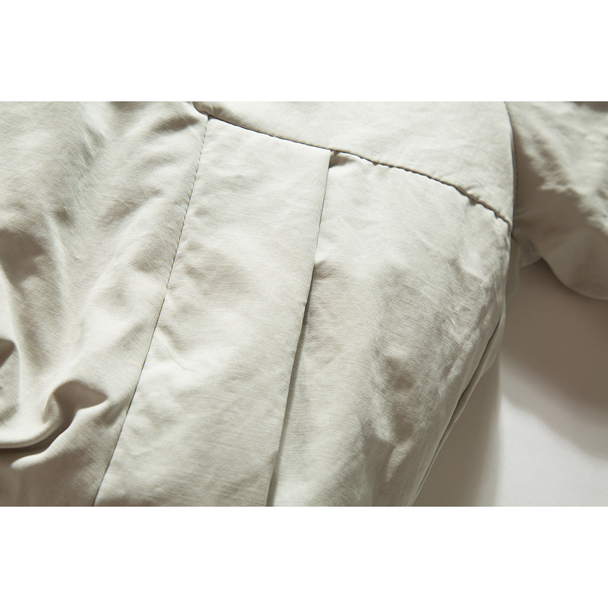 Close-up of a light beige jacket showing a stitched panel seam and fabric texture.
