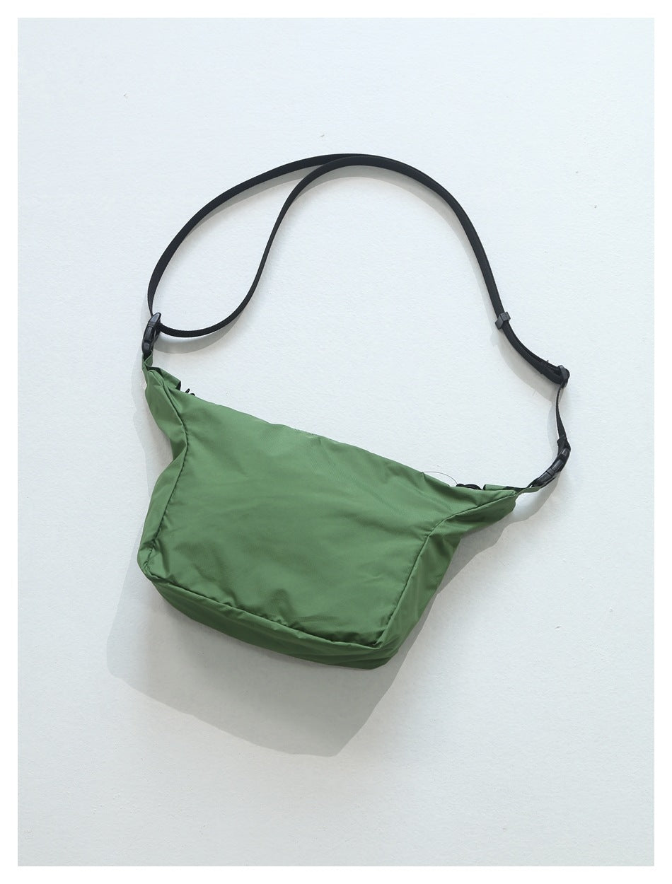 Green crossbody bag with black strap, slider and buckles, flat lay with soft shadow on a light surface