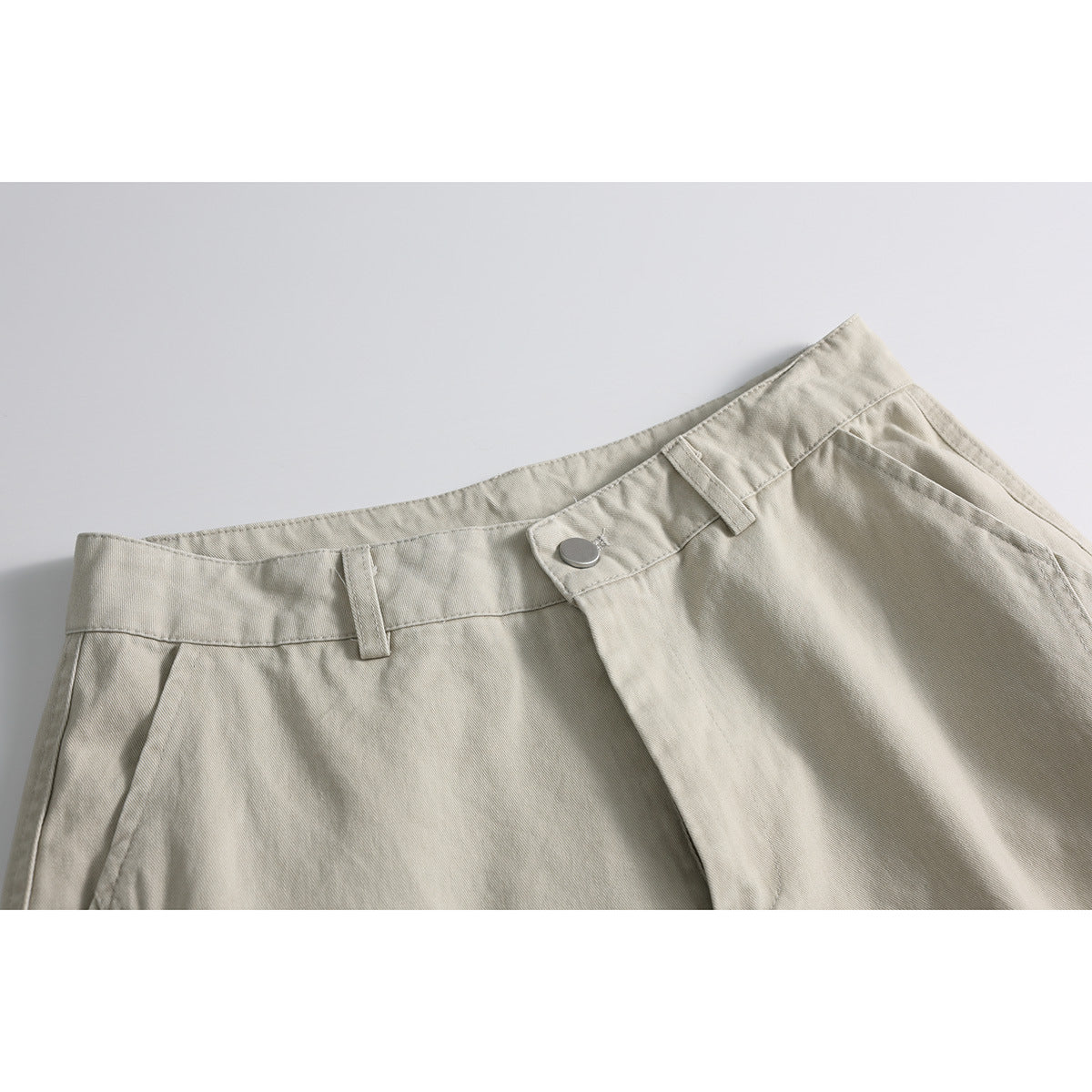 Close-up of light beige shorts showing the waistband, belt loops, metal button and front fly.