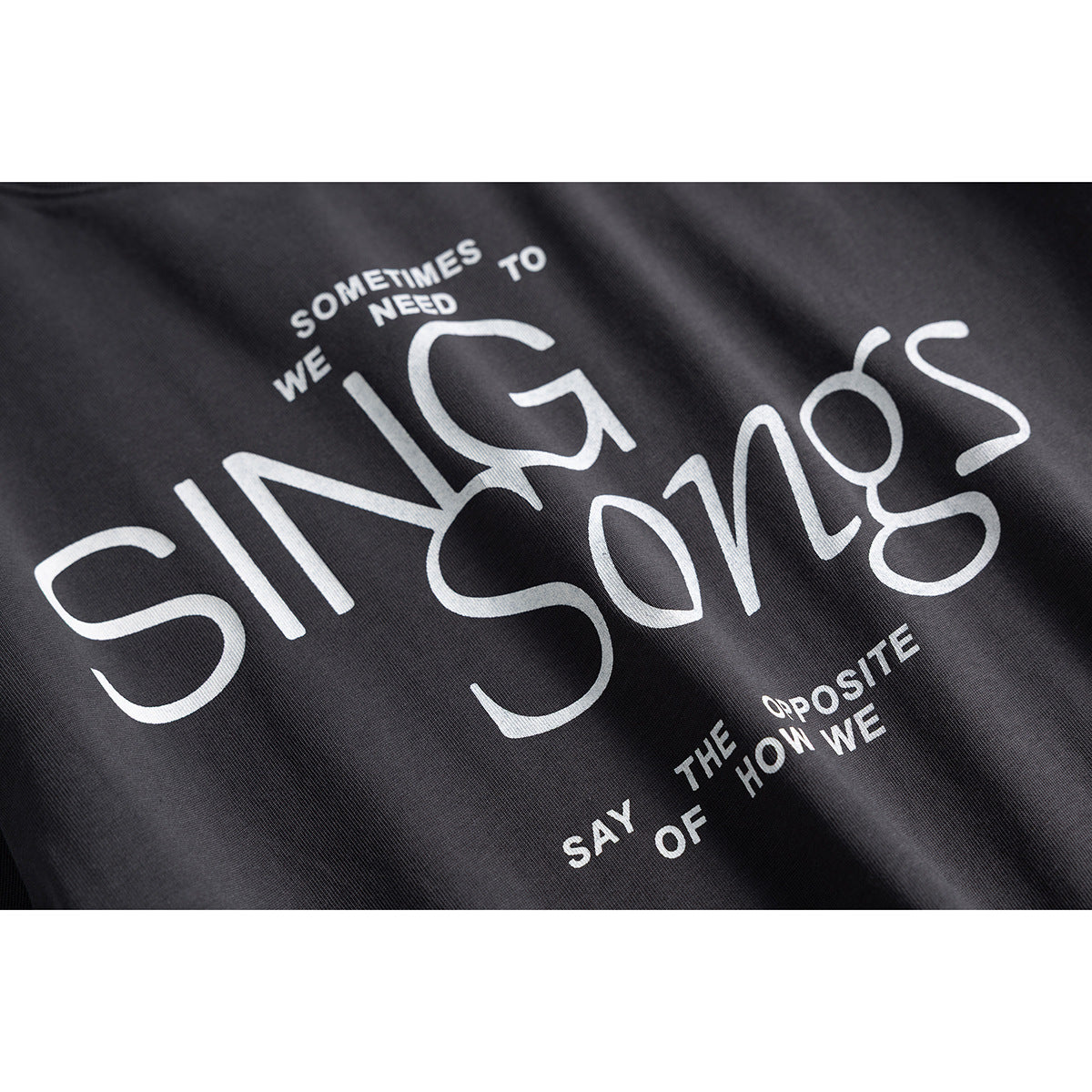 Close-up of a charcoal T-shirt with a large white “SING Songs” graphic and smaller lettering.