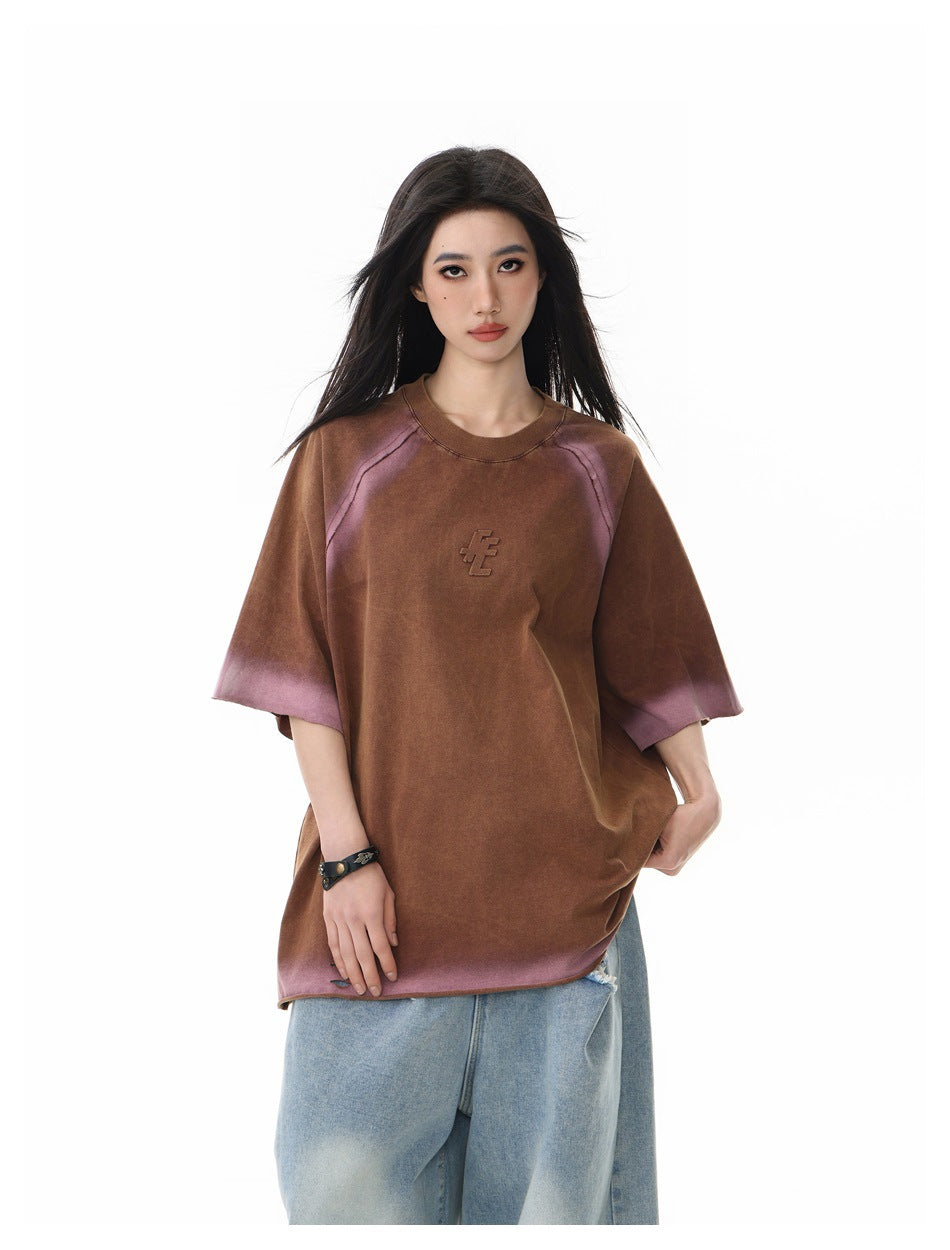 Model wearing an oversized brown T-shirt with muted mauve accents, raglan seams, and a small raised chest emblem.