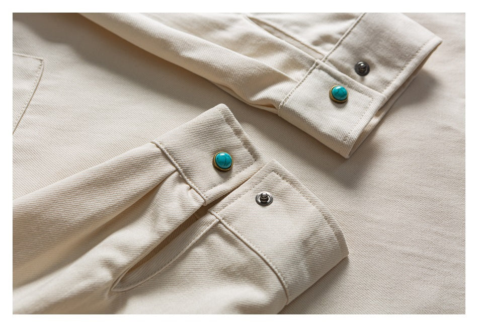 Close-up of light beige garment cuffs with turquoise and dark snap buttons.