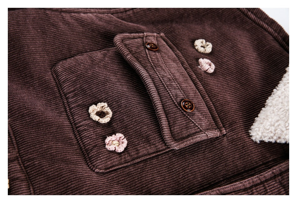 Close-up of a jacket chest pocket, buttoned placket and cream and pink crochet flower accents on plum-brown ribbed fabric.