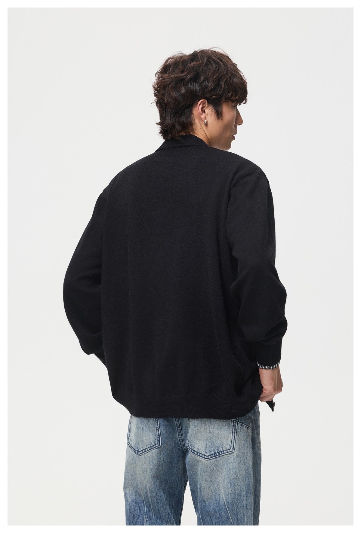 Close back view of a model wearing a black cardigan, with a checked shirt cuff and blue jeans visible.