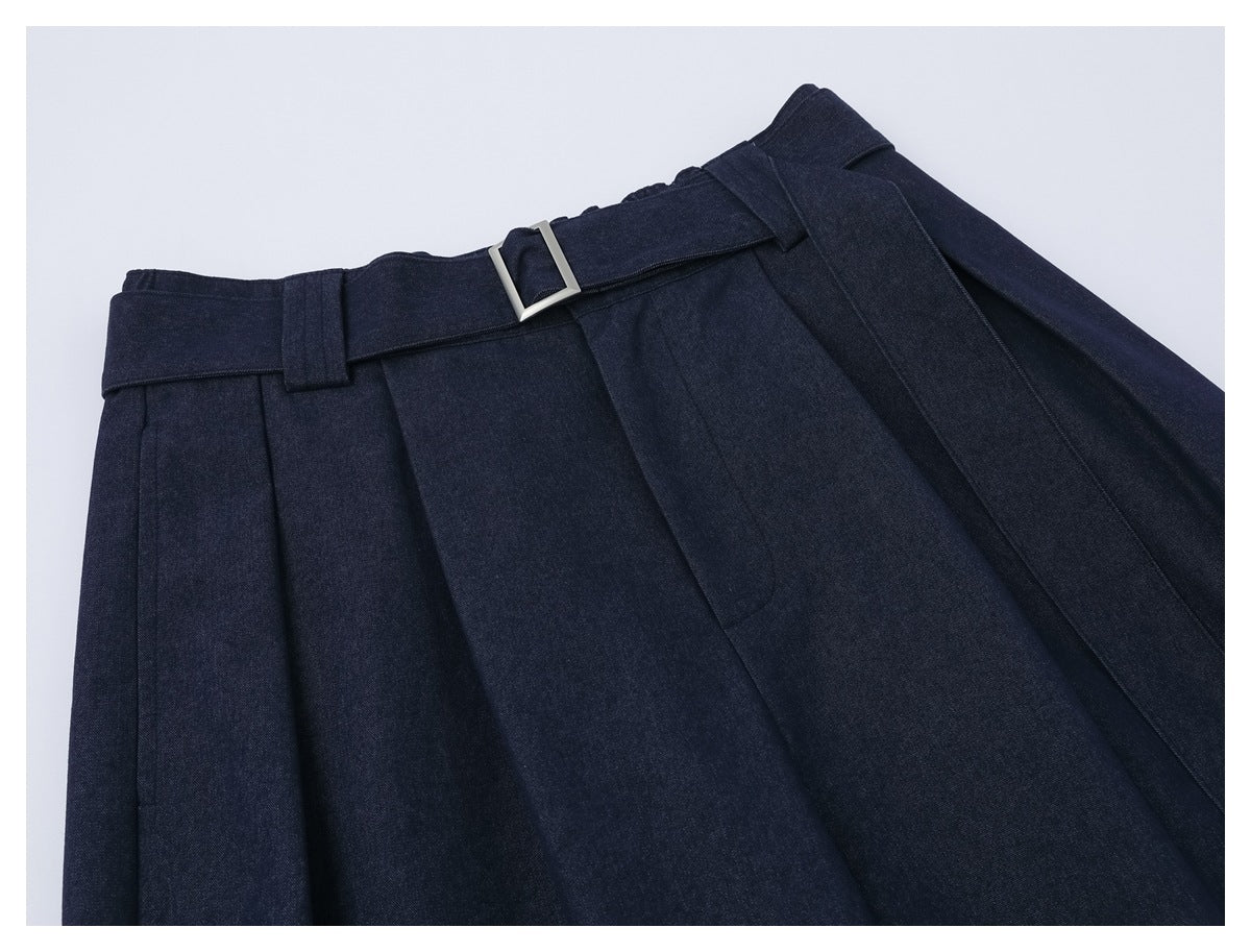 Angled close-up of dark navy trousers showing the pleated waist, matching belt, and rectangular silver buckle.