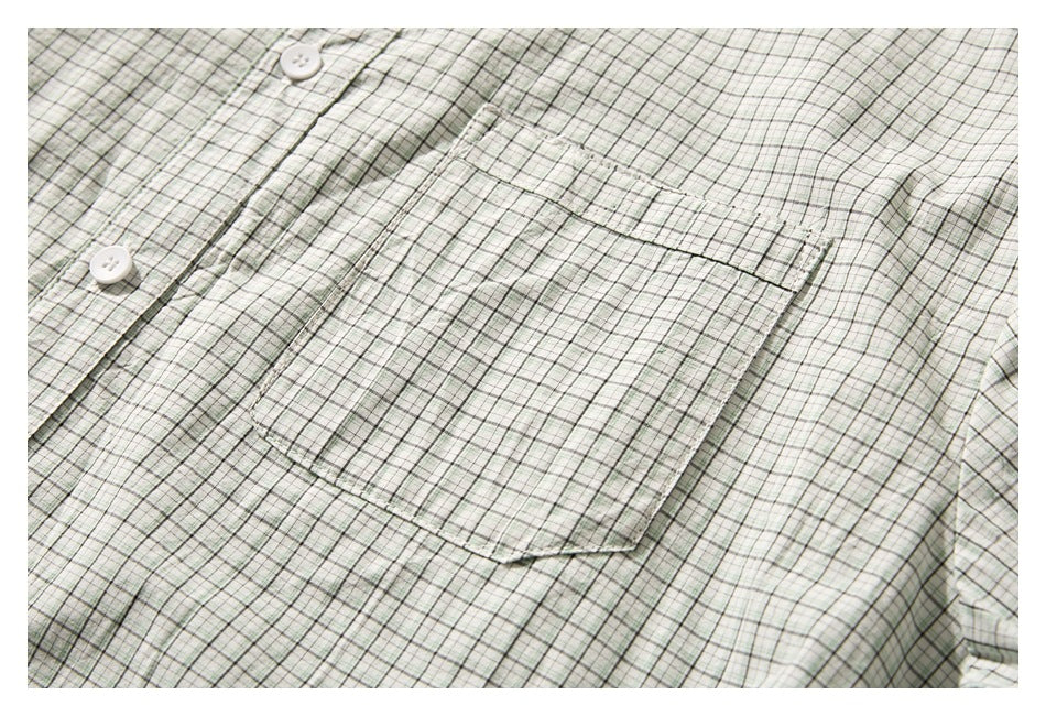 Close-up of a single chest pocket on a pale green and white plaid button-up shirt.