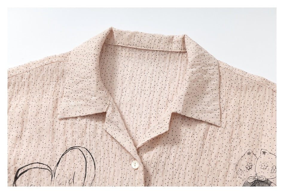 Close-up of the pale blush shirt’s pointed collar, white button, dotted fabric, and partial black illustrations.