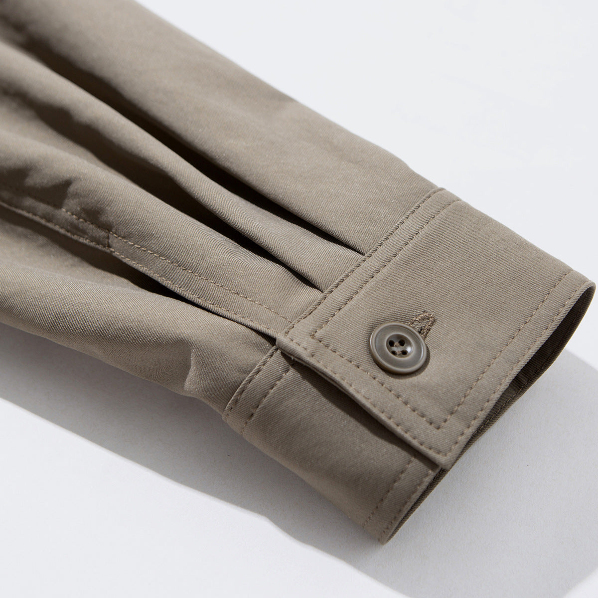 Close-up of a taupe jacket sleeve cuff with a button closure and stitched seams.