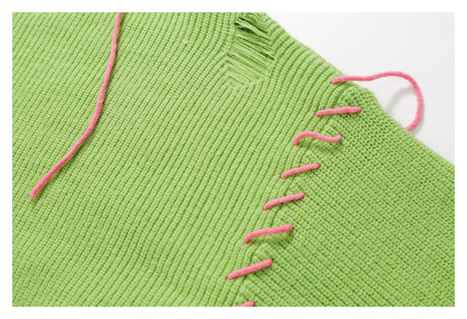 Close-up of lime green knitwear with a seam decorated by loose, bright pink yarn stitches.