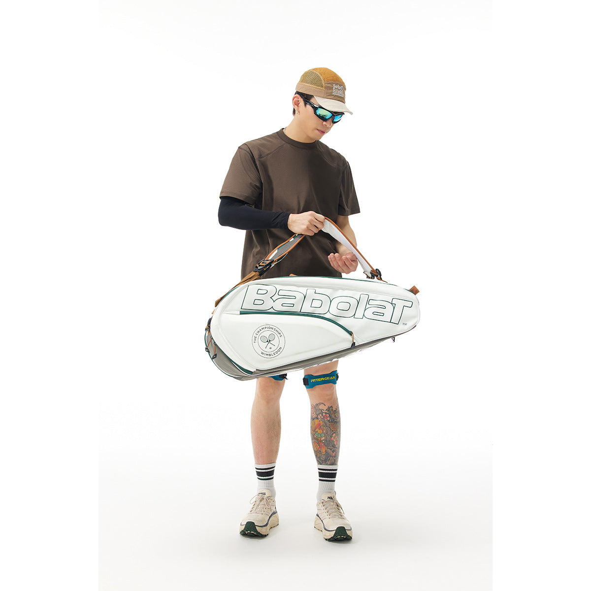 Model wearing a brown short-sleeve T-shirt, partly obscured by a large white tennis bag.