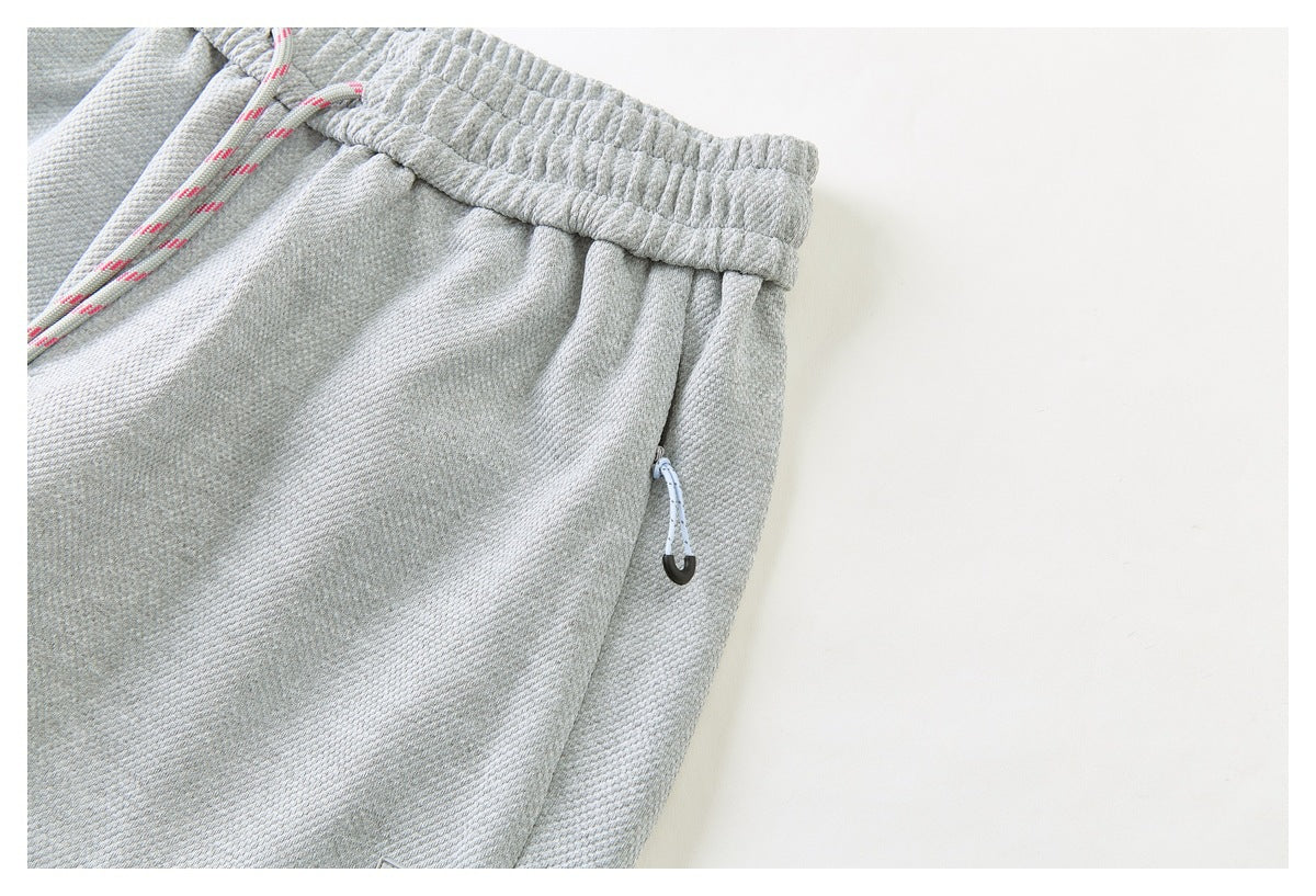Close-up of a zippered side pocket and drawstring waistband on light gray pants.