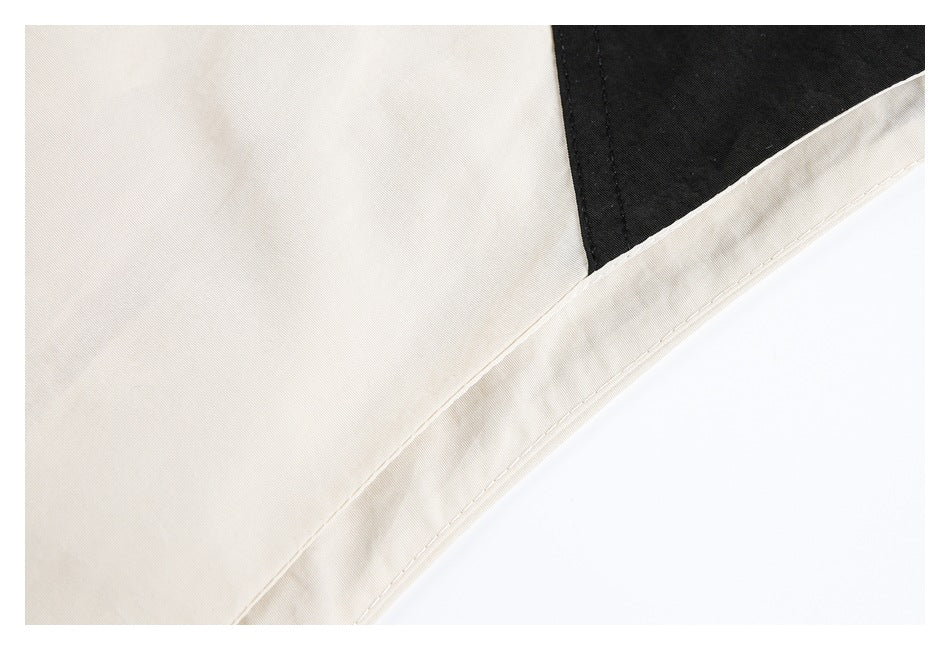 Close-up of a cream jacket's stitched hem and seam beside a black contrast panel.