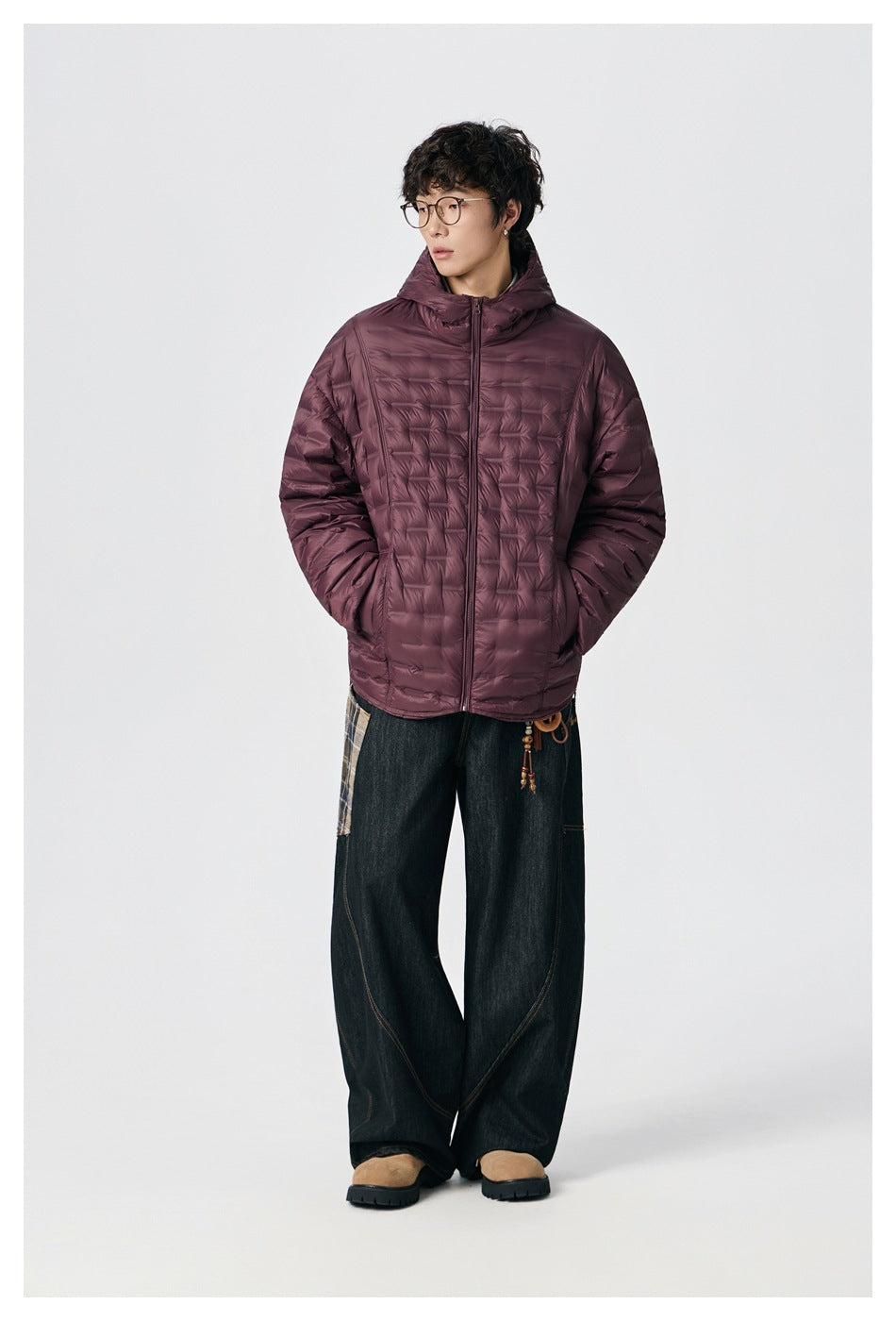Full-length view of a model wearing a burgundy hooded puffer jacket with wide dark jeans and boots