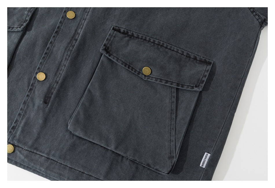 Close-up of a charcoal jacket's large snap-flap pocket, brass front snaps, and small sewn label.