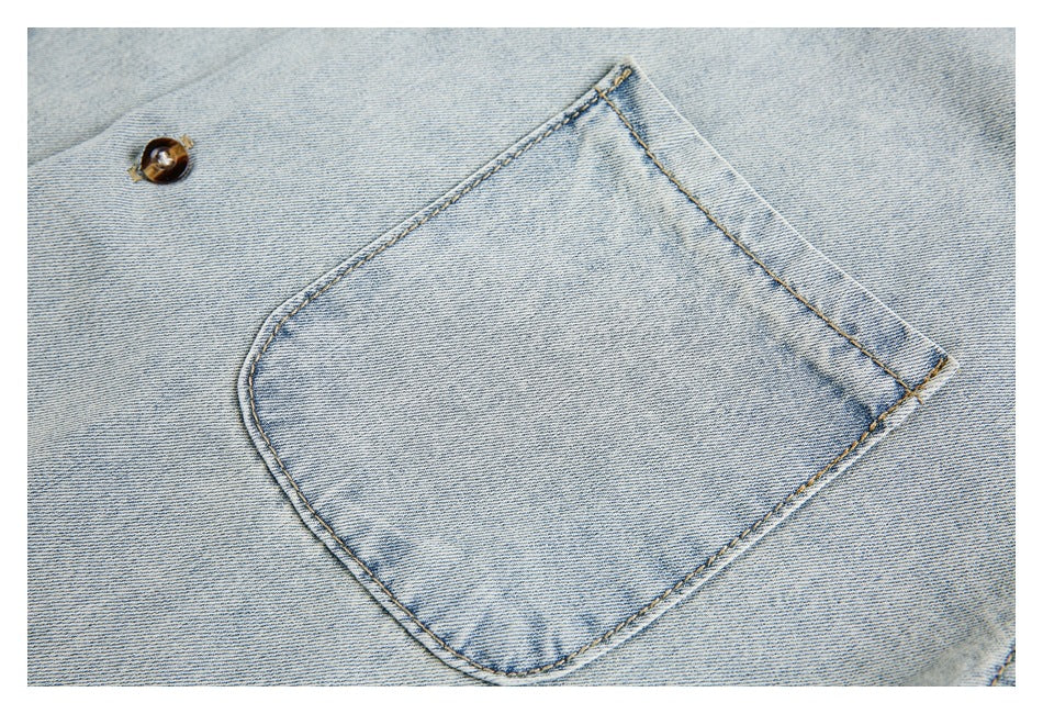 Close-up of a rounded patch pocket and brown button on pale washed denim.