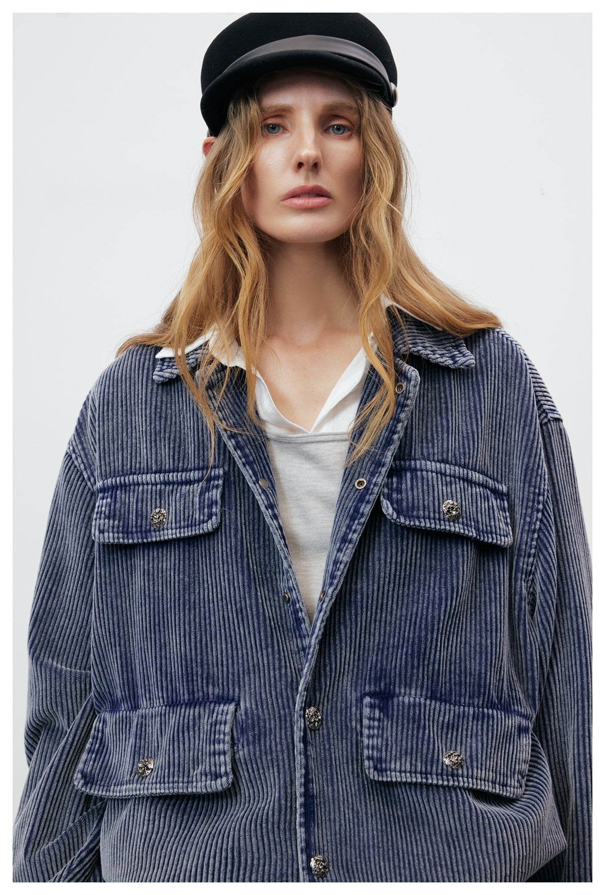 Close-up of a blue ribbed jacket on a model, showing its collar, button placket, and four flap pockets.