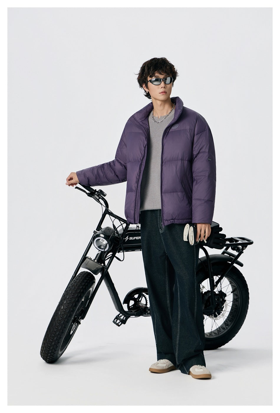 Full-length model wearing an open purple quilted puffer jacket with a high collar and side pockets.