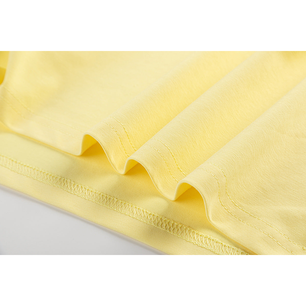Close-up of the pale yellow T-shirt hem, showing folded fabric and overlock stitching.
