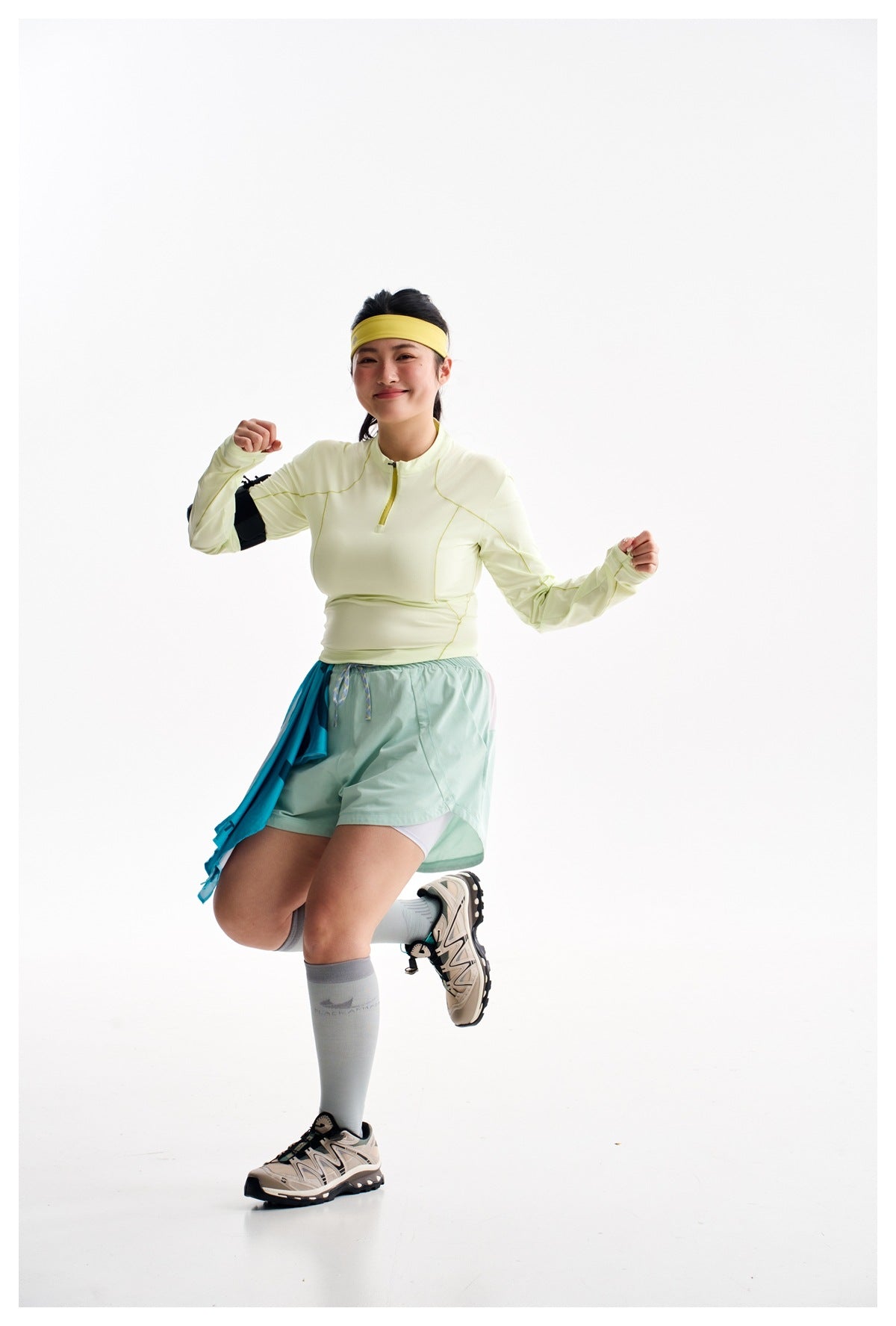 Model posing in a pale yellow long-sleeve quarter-zip top and mint shorts, with a blue towel at her hip.